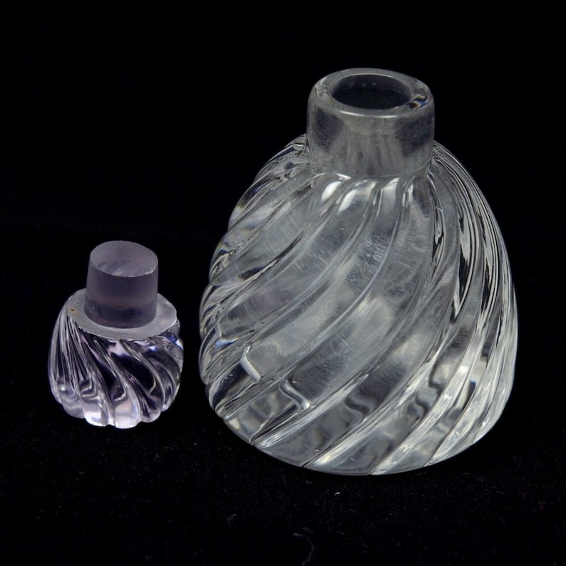 May include: A clear glass bottle with a swirling design and a matching stopper. The bottle is empty and has a round shape.