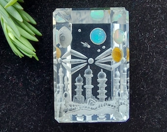 May include: A clear glass pendant with an etched design of a city skyline with buildings and a crescent moon. The pendant has a blue and yellow iridescent finish.
