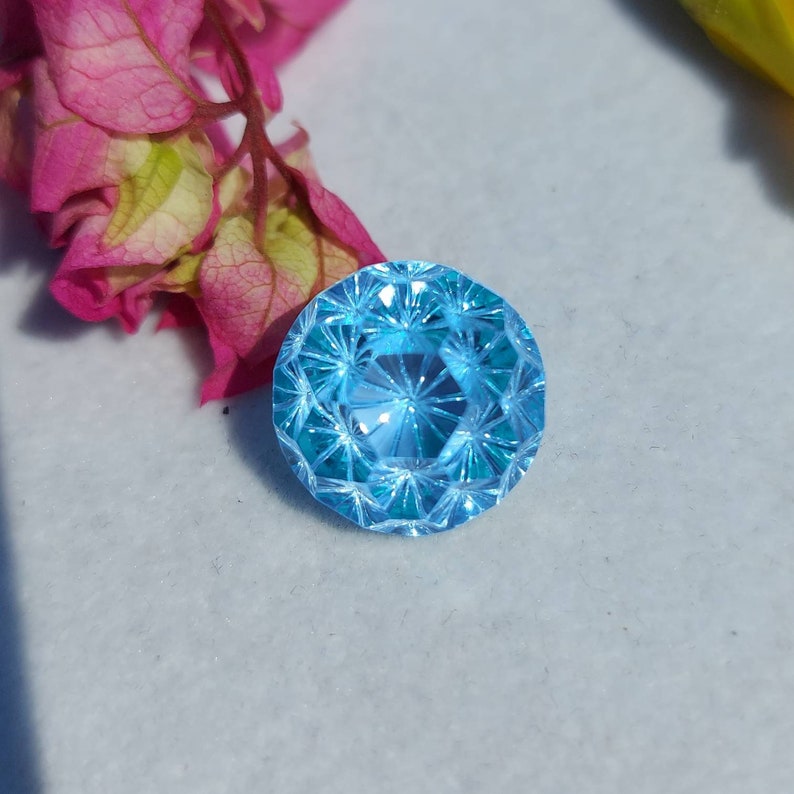 May include: A bright blue gemstone with a faceted cut. The gemstone is round and has a starburst pattern.