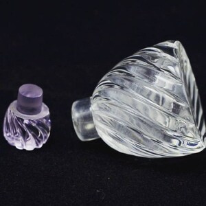 May include: A clear glass bottle with a textured, swirling design. The bottle has a separate, clear glass stopper with a purple hue.