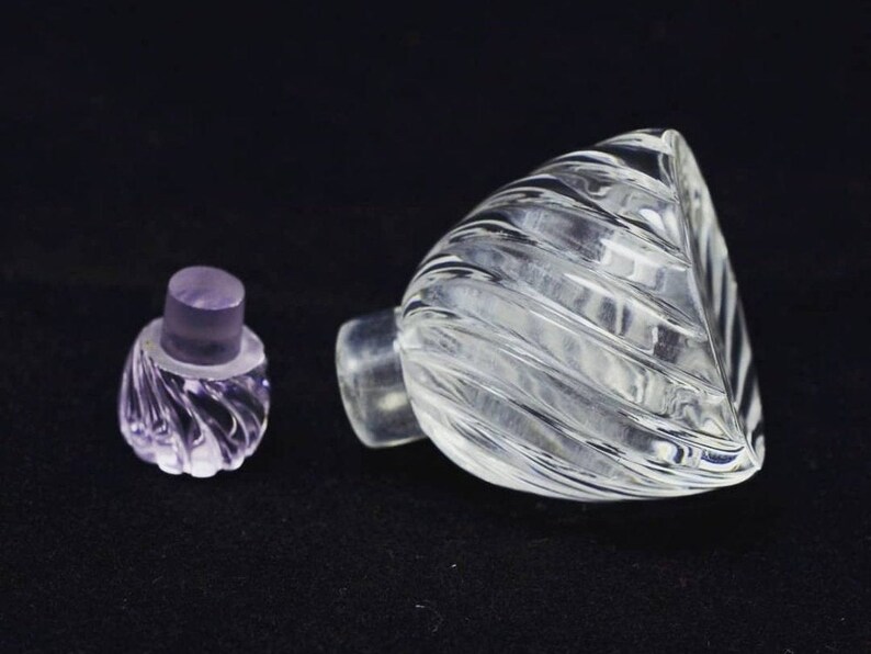 May include: A clear glass bottle with a textured, swirling design. The bottle has a separate, clear glass stopper with a purple hue.