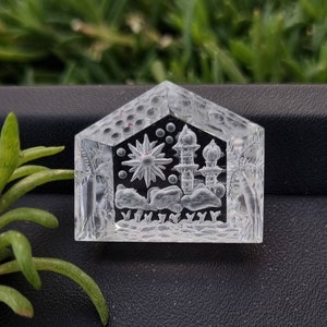 May include: A clear glass paperweight with an intricate design of a star, a building with domes, and palm trees. The design is etched into the glass.