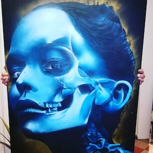 May include: A blue and white painting of a woman's face with a skull overlay. The woman's face is painted in a realistic style, while the skull is more stylized. The painting is done on a canvas and is framed.