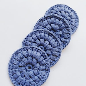 May include: Five blue crocheted cotton rounds, stacked on top of each other. The rounds are made with a textured stitch that resembles a flower.