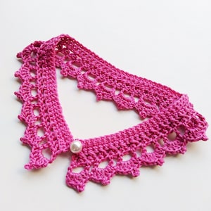 May include: A pink crocheted collar with a pearl accent. The collar is made of delicate crocheted lace and has a scalloped edge.