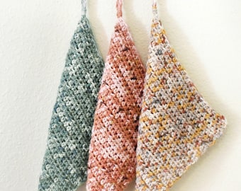 May include: Three crocheted dishcloths hanging on hooks. The dishcloths are in shades of green, pink, and brown.