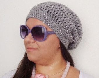 Puede incluir: Un gorro gris de punto con lentejuelas, usado por una persona con cabello largo y castaño. La persona lleva una camisa blanca y un collar de perlas rosa y blanco con un lazo rosa.