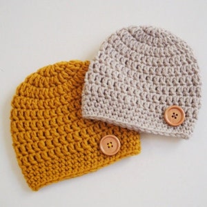 May include: Two crocheted hats with wooden buttons. One hat is mustard yellow and the other is beige.