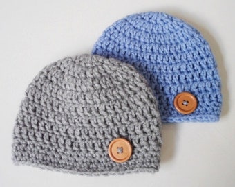 May include: Two crocheted hats with buttons. One hat is gray and the other is light blue.