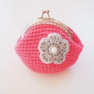 May include: A bright pink crocheted coin purse featuring a metallic gold-tone kiss-lock clasp. The front of the purse is decorated with a light gray crocheted flower applique, which has a small white pearl bead centered in the middle of the petals.