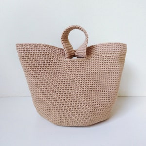 May include: A beige crocheted tote bag with a single loop handle.