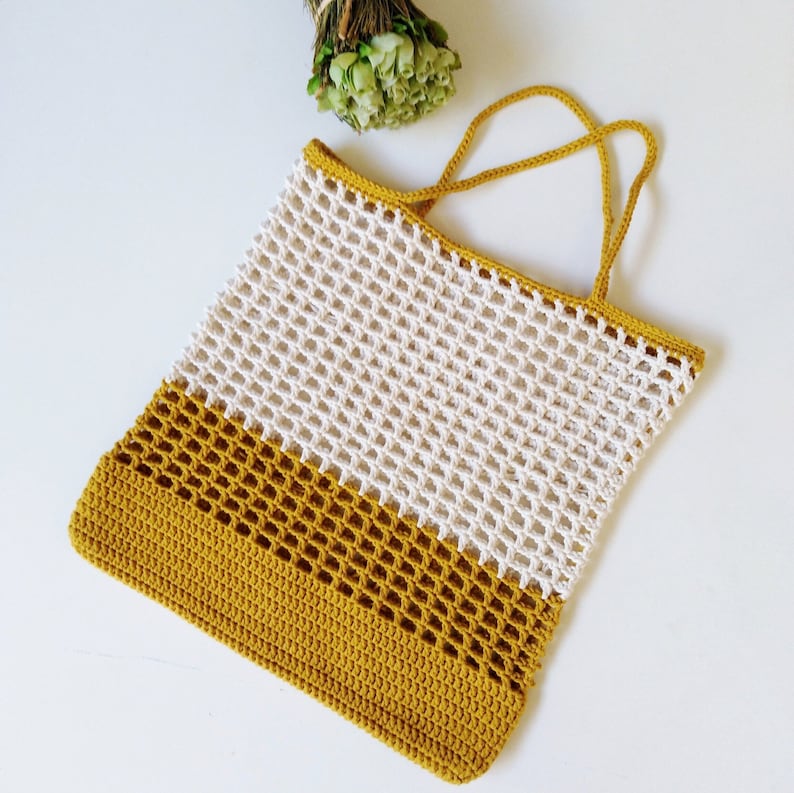 May include: A crocheted tote bag with a white top section and a mustard yellow bottom section. The bag has a wide, open top and two handles.