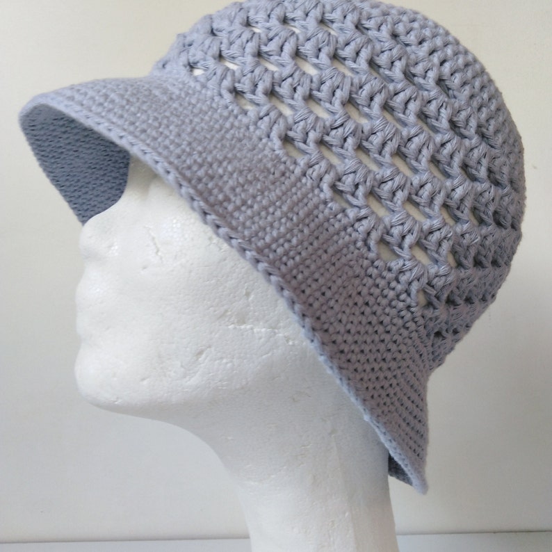 Peut inclure: Un chapeau en crochet gris clair de forme seau avec un large bord et un motif en tissage ouvert.