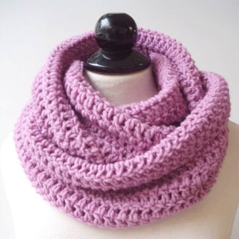 May include: A soft, purple knitted infinity scarf. The scarf is made of a chunky yarn and has a simple, textured design.