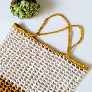 May include: A white crocheted mesh bag with a mustard yellow crocheted handle. The bag is a rectangular shape with a wide opening.