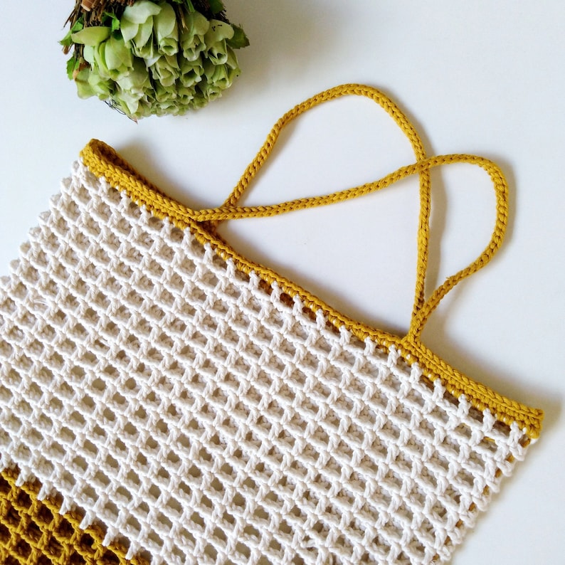 May include: A white crocheted mesh bag with a mustard yellow crocheted handle. The bag is a rectangular shape with a wide opening.