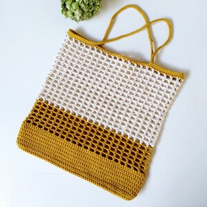May include: A crocheted tote bag with a white and mustard yellow color scheme. The bag has a wide, flat base and a single handle.