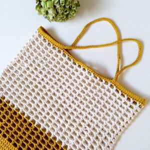 May include: A white and mustard yellow crocheted tote bag with two handles. The bag is made with a simple grid pattern.