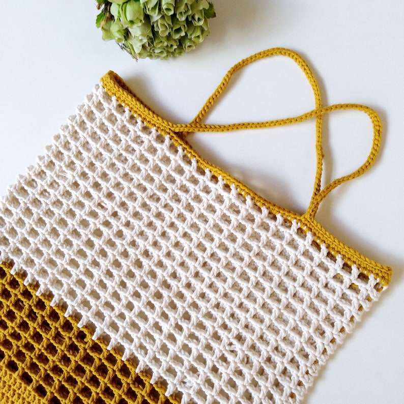 May include: A white and mustard yellow crocheted tote bag with two handles. The bag is made with a simple grid pattern.