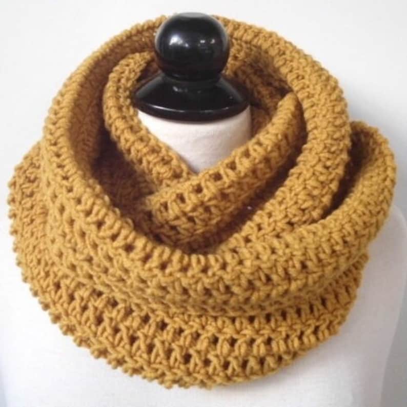 May include: A mustard yellow crocheted infinity scarf. The scarf is made with a simple stitch pattern and is thick and warm.
