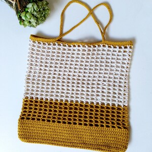 May include: A white and mustard yellow crocheted tote bag with a mesh design. The bag has two handles.