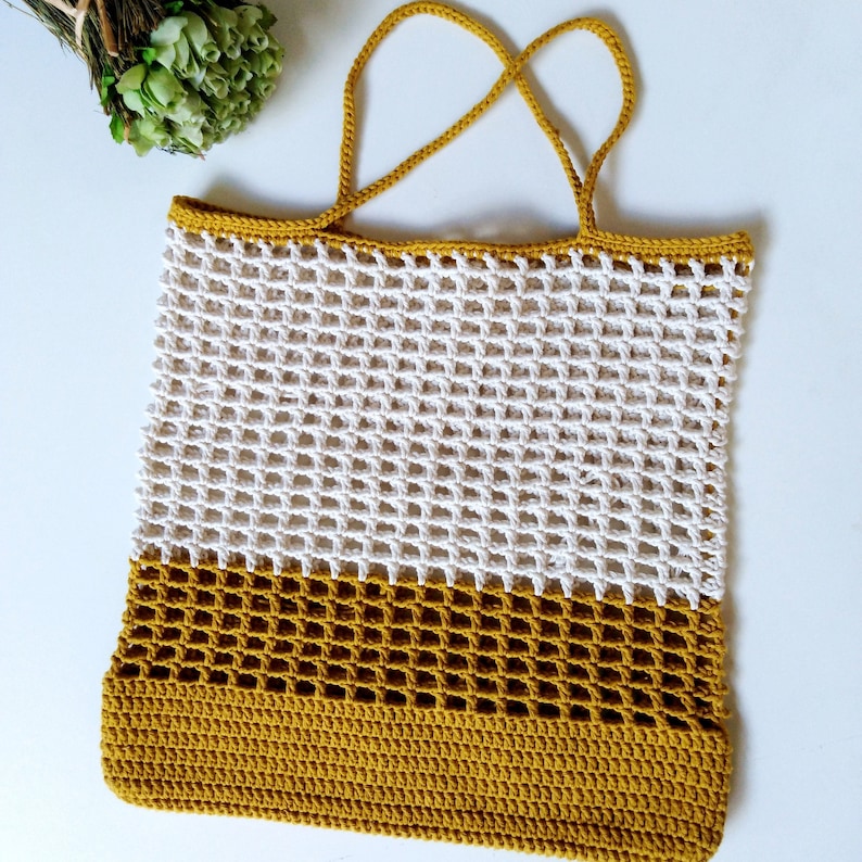 May include: A white and mustard yellow crocheted tote bag with a mesh design. The bag has two handles.
