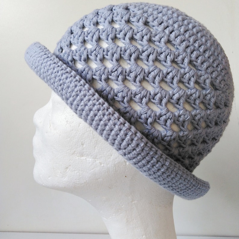 Peut inclure: Un chapeau crochet&eacute; gris avec un large bord et un motif ajour&eacute;. Le chapeau est fait avec un fil gris clair et a un style simple et classique.