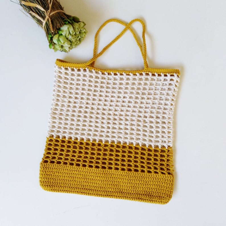May include: A crocheted tote bag with a white top section and a mustard yellow bottom section. The bag has a wide, open top and two long handles.