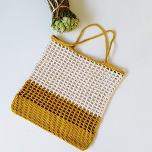 May include: A crocheted tote bag with a white and mustard yellow color scheme. The bag has a wide, open top and two handles.