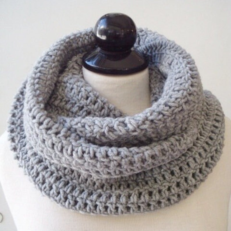 May include: A gray crocheted infinity scarf. The scarf is made with a simple stitch pattern and is thick and warm.
