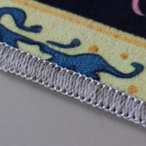 Op de afbeelding: Close-up van een grijze stoffen rand met een wit stikdetail. De stof is geweven en heeft een textuur.