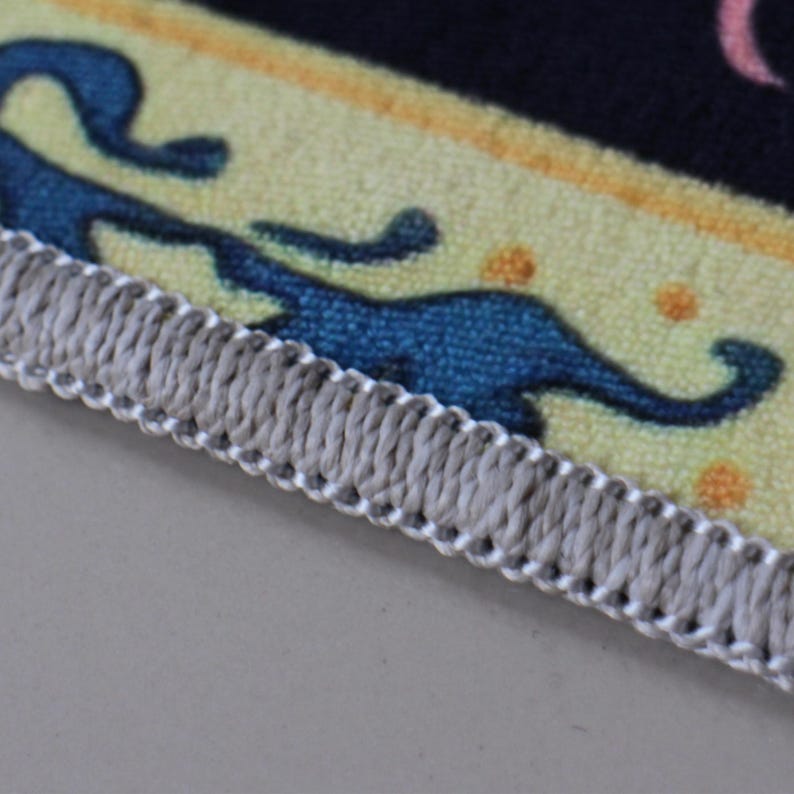 Op de afbeelding: Close-up van een grijze stoffen rand met een wit stikdetail. De stof is geweven en heeft een textuur.