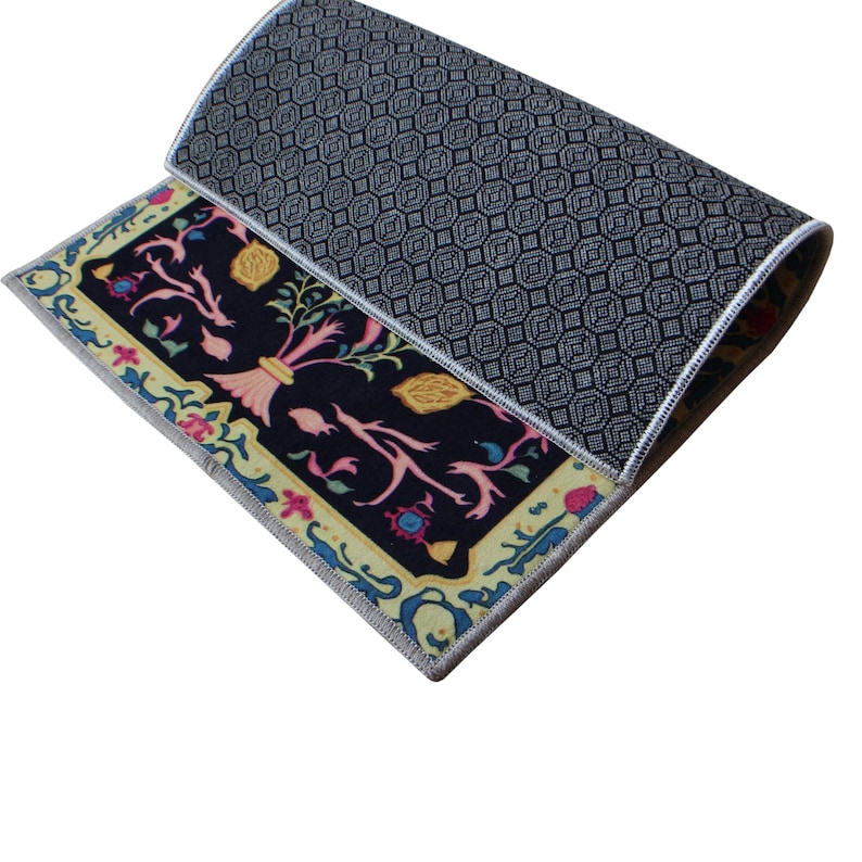 Op de afbeelding: Een zwart en geel tapijt met een bloemenpatroon. Het tapijt heeft een zwart-wit geometrisch patroon aan de achterkant.