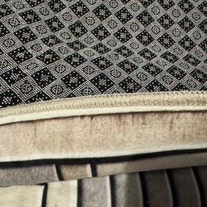 Op de afbeelding: Close-up van een zwart-wit gepatroneerd tapijt met een beige rand. Het tapijt heeft een dikke, pluche textuur.