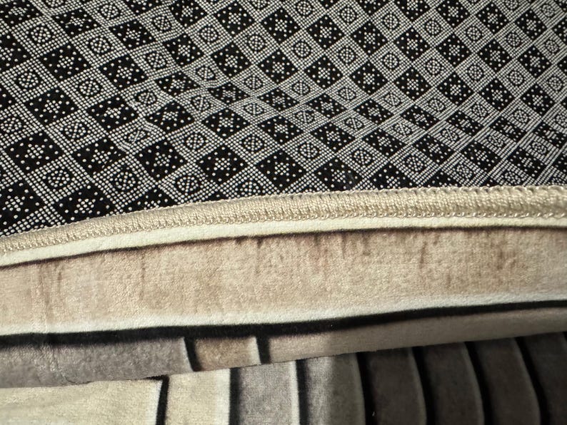 Op de afbeelding: Close-up van een zwart-wit gepatroneerd tapijt met een beige rand. Het tapijt heeft een dikke, pluche textuur.