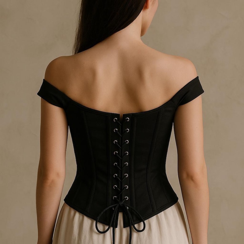 May include: Black off-the-shoulder corset with a lace-up back. The corset has a structured design with vertical seams and a curved neckline. The back features a series of eyelets for the lacing, and the bottom of the corset is slightly flared.