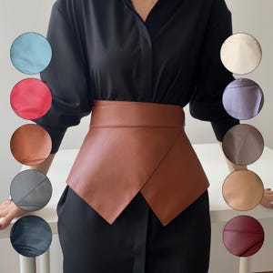 May include: A brown leather wrap belt with an asymmetrical design. The belt is shown on a person wearing a black shirt. The image also displays a color palette of leather swatches in various colors, including blue, red, and cream.