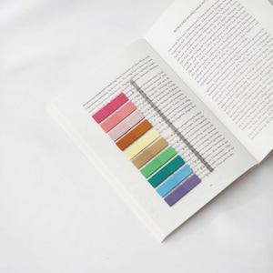 Può includere: Un libro aperto con segnalibri adesivi colorati. I segnalibri sono in un arcobaleno di colori, tra cui rosa, arancione, giallo, verde, blu e viola. Un righello trasparente è anche sulla pagina.