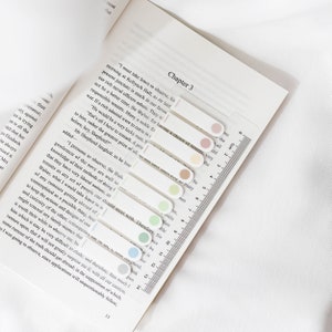 May include: A book is open to Chapter 3, with several clear, rectangular page markers with colored circles at the top. A clear ruler with centimeter markings is on the right side of the book.