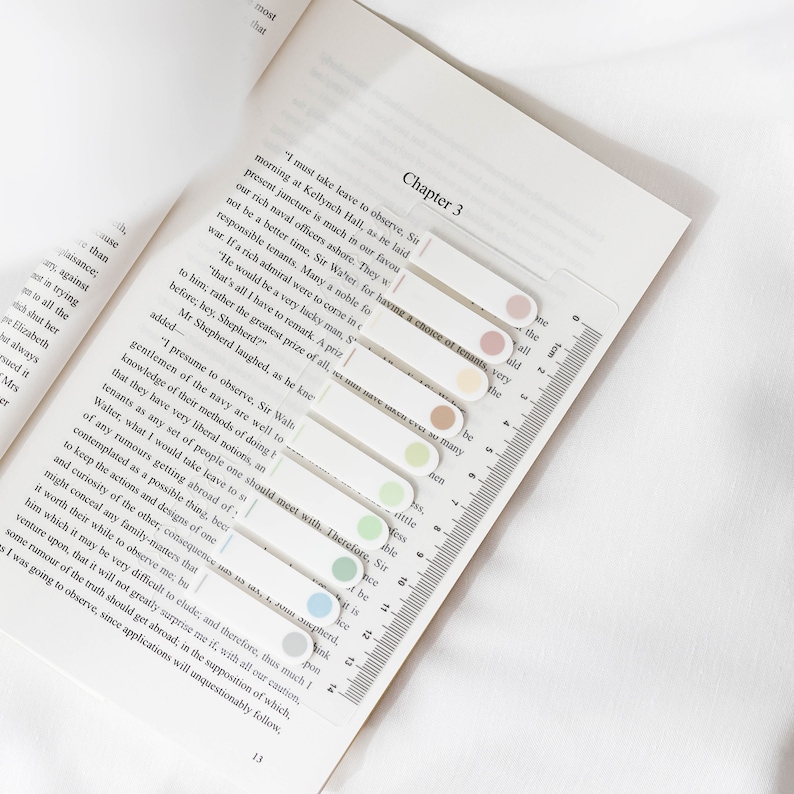 May include: A book is open to Chapter 3, with several clear, rectangular page markers with colored circles at the top. A clear ruler with centimeter markings is on the right side of the book.