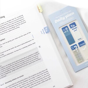Könnte beinhalten: Ein blauer und weißer Tagesplaner mit Checklisten- und To-Do-List-Aufklebern. Die Aufkleber haben einen blauen Hintergrund mit weißem Text und Häkchen. Der Planer hat den Text "Daily Plan" auf der Vorderseite.