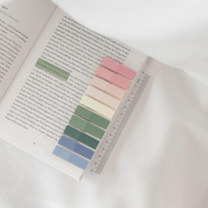 Könnte beinhalten: Nahaufnahme eines Lineals mit verschiedenen bunten Haftnotizen. Die Notizen sind in den Farben Rosa, Gelb, Grün und Blau. Das Lineal ist in Zentimetern gekennzeichnet.