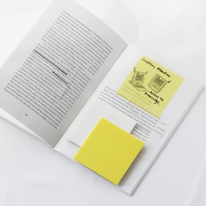 Könnte beinhalten: Ein offenes Buch mit Text und einem gelben Haftzettel mit der Aufschrift "Children's Machine" mit einer Zeichnung eines Laptops und eines Tablets. Ein zweiter gelber Haftzettel befindet sich im Vordergrund.