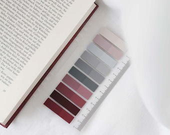 May include: A set of colorful sticky notes in shades of pink, gray, and red. The notes are arranged in a row on a white surface with a ruler.