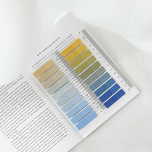 Op de afbeelding: Een boek dat open ligt op een pagina met tekst over retro-design en een liniaal met kleurstalen in geel, groen, blauw en lichtblauw. De kleurstalen zijn gelabeld met de kleurnamen in het Duits.