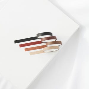 Op de afbeelding: Vijf rollen washi tape in verschillende bruintinten, waaronder zwart, donkerbruin, middelbruin, lichtbruin en beige. De tape is gestapeld, met de zwarte tape bovenop en de beige tape onderaan.