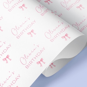 May include: White wrapping paper with a repeating pattern of pink bows and the text "Olivia's Birthday".