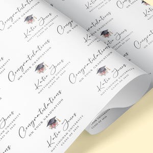 May include: White wrapping paper printed with graduation-themed text and graphics. The design includes the words "Congratulations," "Katie Jones," and "Nottingham University Class of 2026," along with a graduation cap and floral accents.