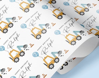 May include: White wrapping paper with a repeating pattern of yellow construction vehicles with blue balloons that say "Happy Birthday Ralph" on them.