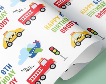 May include: White wrapping paper with a repeating pattern of a yellow taxi, a red fire truck, a blue airplane, and a green traffic light. The text "Happy 6th Birthday Brody" is repeated throughout the pattern.